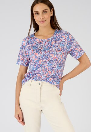 Camiseta de manga corta en un patrón floral azul, rosa y blanco. Cuello redondo con un corte relajado, combinada con pantalones beige claros.