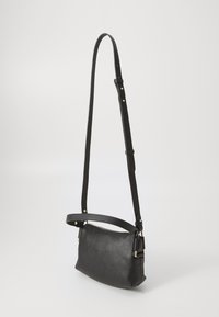 Borsa a tracolla in pelle nera con finitura testurizzata, tracolla regolabile e hardware in tonalità dorata. Forma compatta con chiusura a zip superiore.