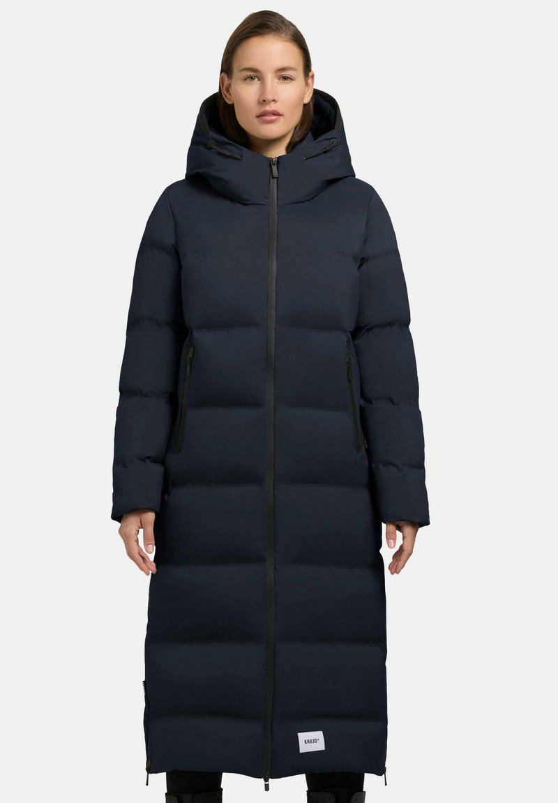 Giacca a vento blu navy di lunghezza lunga, con cappuccio e chiusura con zip. Presenta un design trapuntato, due tasche laterali e un logo in evidenza all'orlo.