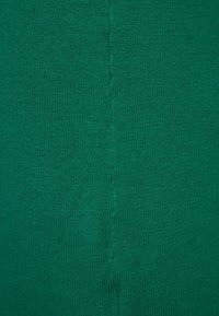 Gros plan sur un tissu tricoté vert montrant une couture verticale avec des points réguliers au centre.