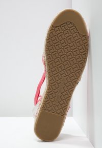 Suela de esparto en tonos rosa y beige con un patrón intrincado, superficie texturizada y detalles de marca; cuenta con una delgada correa rosa adjunta.