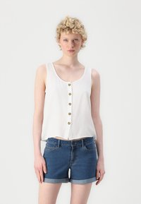 Hvit ermeløs bluse med rund hals og frontknapper, kombinert med blå denimshorts med brettede oppkant og sidelommer.
