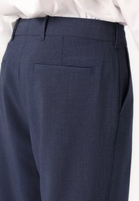 Pantalones navy confeccionados en tejido texturizado, con un corte entallado, dos bolsillos laterales y un bolsillo trasero para un detalle adicional.