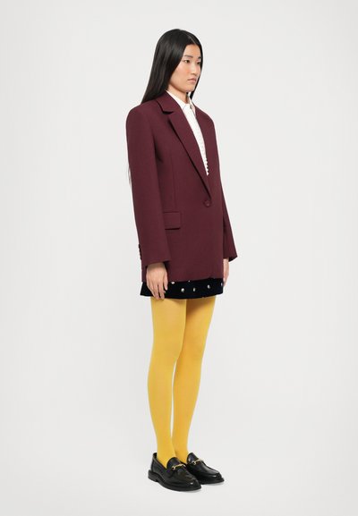 Burgundy oversized blazer over a white lace shirt, paired with a black velvet skirt, yellow tights, and black loafers with gold hardware accents.