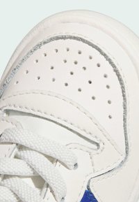 White leather sneaker featuring perforated detail on the toe, textured laces, and a blue accent on the side with visible stitching.