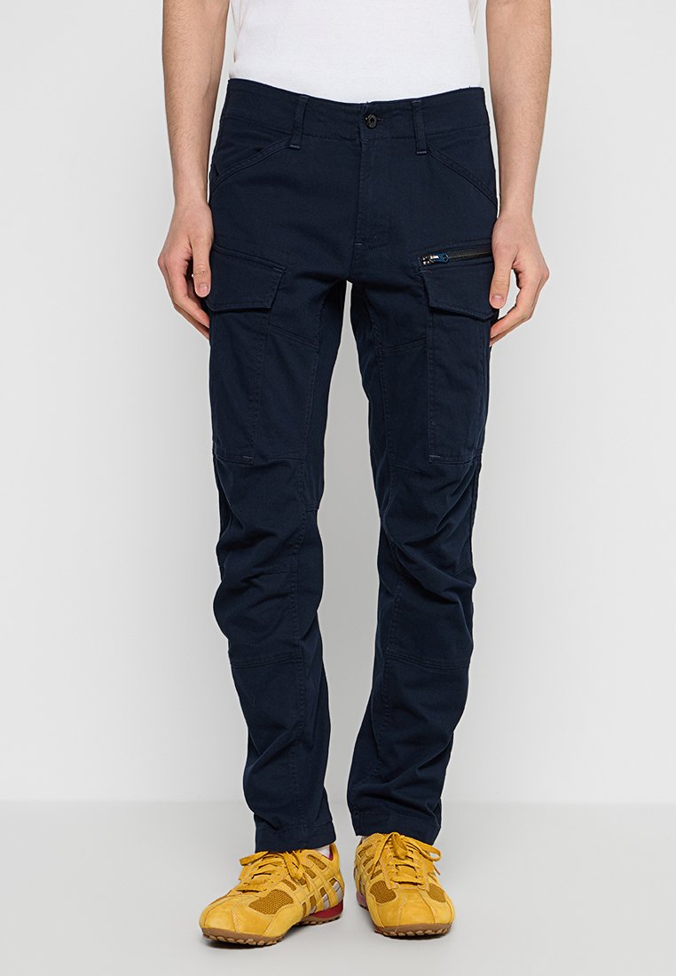 Marine Cargo-Hosen aus einem Baumwollmischgewebe, ausgestattet mit seitlichen Taschen und einer Reißverschlusstasche. Das Design umfasst eine enganliegende Silhouette und Knöchelbündchen.