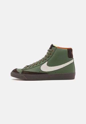 Baskets montantes vertes avec virgule Nike blanche, semelle marron, bout marron et doublure intérieure orange, vues de côté sur fond blanc.