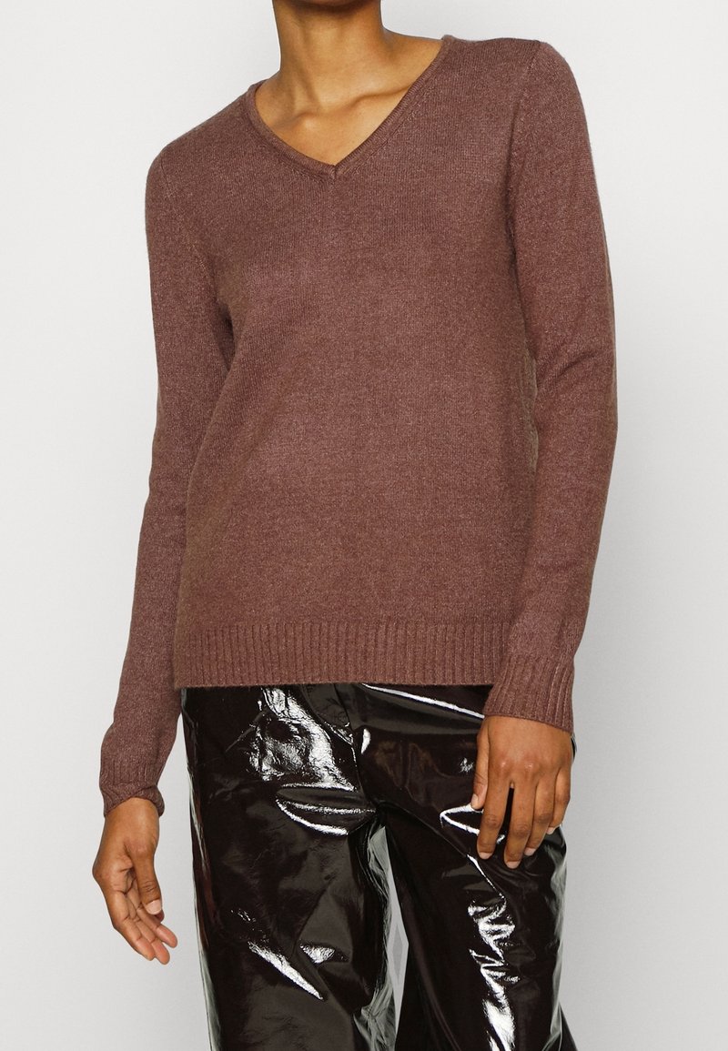 Brun v-ringad tröja i mjukt material, med långa ärmar och ribbade muddars, kombinerad med glänsande svarta byxor. Enkel, figurnära design.