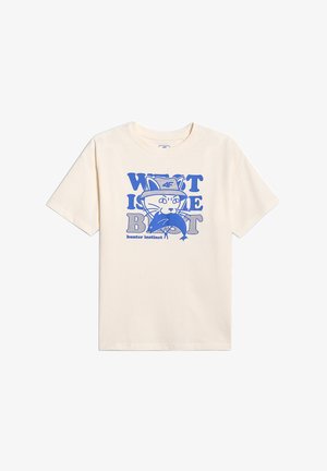 T-shirt écru avec une illustration bleue d’un chat portant un chapeau tenant un poisson, avec le texte « What is the beat » et « hunter instinct ».
