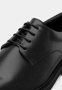 Μαύρο δερμάτινο παπούτσι με λεία επιφάνεια, σχέδιο με οκτώ τρύπες για κορδόνια και στρογγυλεμένη μύτη. Λεπτές ραφές κατά μήκος των ραφών.