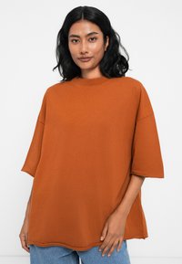 Καφέ φαρδύ t-shirt φτιαγμένο από μαλακό βαμβάκι με κοντά μανίκια και στρογγυλή λαιμόκοψη, με χαλαρή εφαρμογή και λεπτομέρειες ραφής.