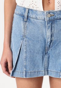 Lichtblauwe denim rok met een rechte snit, een sluiting met knopen aan de voorkant en zijplooidetails. De stof heeft een vervaagde textuur met zichtbare stiksels.