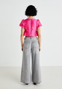 Rozā īsā blouse ar strukturētu ziedu rakstu un pūkainām piedurknēm, apvienota ar pelēkām denimba biksēm ar augstu jostasvietu un platu kāju.