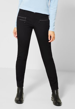 Zwarte slim-fit broek gemaakt van zachte stof, met twee ritszakken aan de voorkant en een knoopsluiting. Gekomplementeerd met zwarte enkellaarsjes.