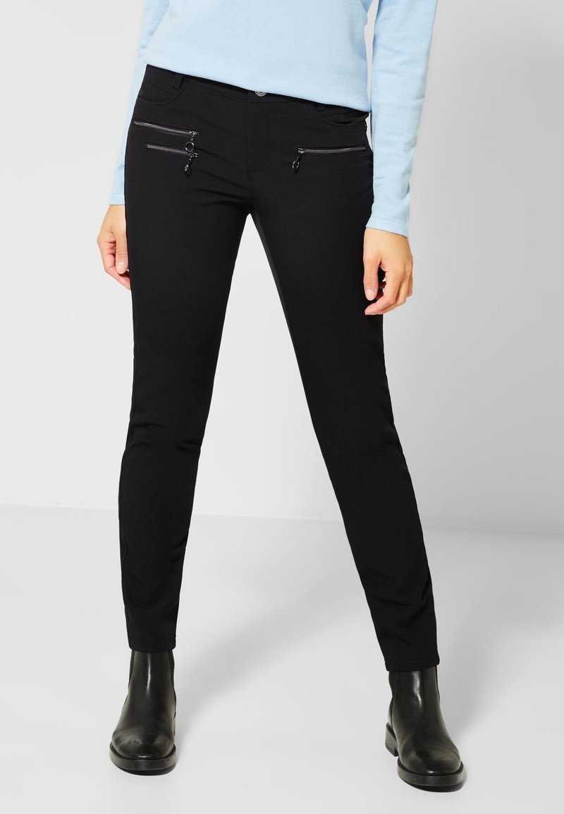 Svarta slim-fit byxor i mjukt tyg, med två framtida fickor med dragkedja och knappstängning. Matchat med svarta ankelboots.