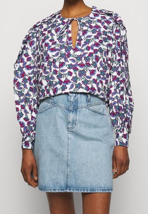 Femme portant un chemisier à manches longues à motif floral avec une encolure keyhole et une mini-jupe en jean bleu clair.