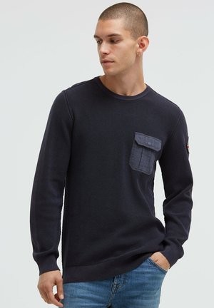 Marineblauer Langarmpullover aus Strick mit Rippenstruktur, rundem Ausschnitt und einer Vorderseite mit einer Tasche aus kontrastierendem dunklem Stoff. Eng anliegende Bündchen und Taillenabschluss.