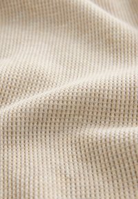 Hellbeige gerippter Stoff mit einer strukturierten Oberfläche, die kleine, regelmäßig verteilte erhabene Muster aufweist, weich und dehnbar.