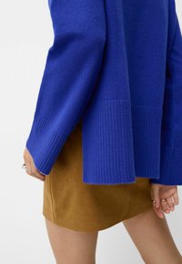 Bright blue knitted sweater with ribbed cuffs, paired with a brown suede skirt, showcasing a smooth texture and simple design.