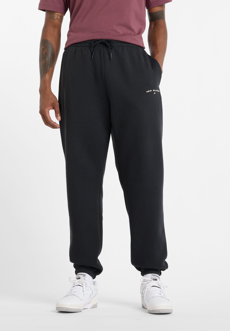 Čierne tepláky s elastickým pásom a detailom na šnúrku. Obsahujú malé zlaté logo "New Balance" na ľavom stehne. Mäkkučká textúra.