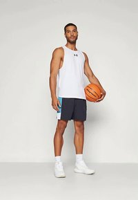 White athletic tank top with a black logo, paired with navy shorts featuring light blue accents. The model holds a basketball and wears white sneakers.