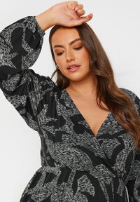 Robe noire avec un motif abstrait blanc audacieux, présentant un décolleté en V profond et de longues manches bouffantes, fabriquée en tissu léger.