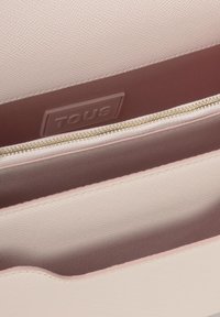 Innerraum einer pinkfarbenen veganen Lederhandtasche mit taupefarbenem Futter und goldener Reißverschluss. Prägung des "TOUS"-Logos an der Wand des Faches.