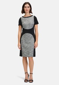 Kurzärmliges Kleid mit schwarzem Grundton, das an der Vorderseite strukturierte graue kreisförmige Muster aufweist. Knielang mit einer figurbetonten Silhouette.