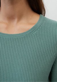 Lysegrøn strikket sweater med ribbet struktur og bred bådudhals, nærbillede der fremhæver stofdetaljer.