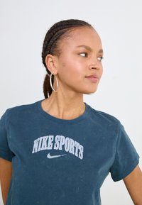 Dark blue cotton T-shirt with "NIKE SPORTS" in white arched lettering. Short sleeves, round neckline, slightly worn texture, featuring a small logo.