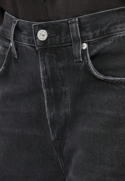 Μαύρο τζιν με ψηλή μέση, με ασημένιο κουμπί, ορατές ραφές και υφή. Το ύφασμα έχει ελαφριά ελαστικότητα.