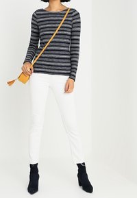 Haut à manches longues rayé noir et blanc, pantalon slim blanc et bottines noires. Un sac bandoulière jaune avec un détail en frange.