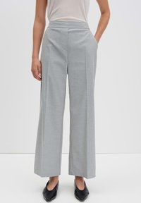 Lichtgrijze wijde broek met een platte tailleband, zijzakken en een gladde textuur, gecombineerd met zwarte instappers.