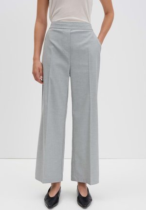 Pantalons larges gris clair avec une taille plate, des poches latérales et une texture lisse, associés à des chaussures noires à enfiler.