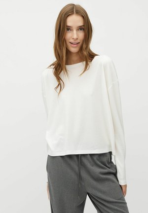 Top alb cu mânecă lungă, cu o croială lejeră, guler rotund și umeri lăsați, asortat cu pantaloni de tip jogger în nuanță de gri, cu șnur.