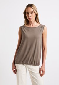 Top marrone senza maniche con scollatura a girocollo e dettaglio arricciato sulle spalle, stretto all'orlo per una vestibilità rilassata, abbinato a pantaloni bianchi.