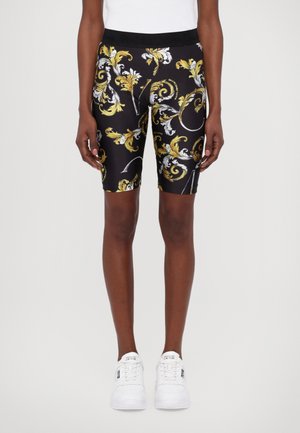 Shorts da ciclismo neri con un motivo floreale ornamentale giallo e bianco; design aderente con vita elasticizzata; abbinati a sneakers bianche.