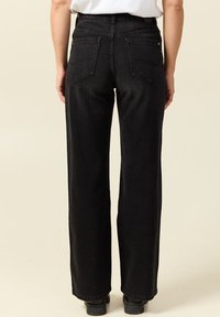 Pantalones de mezclilla anchos negros con cintura alta, que presentan dos bolsillos traseros con costuras curvas y un acabado texturizado.