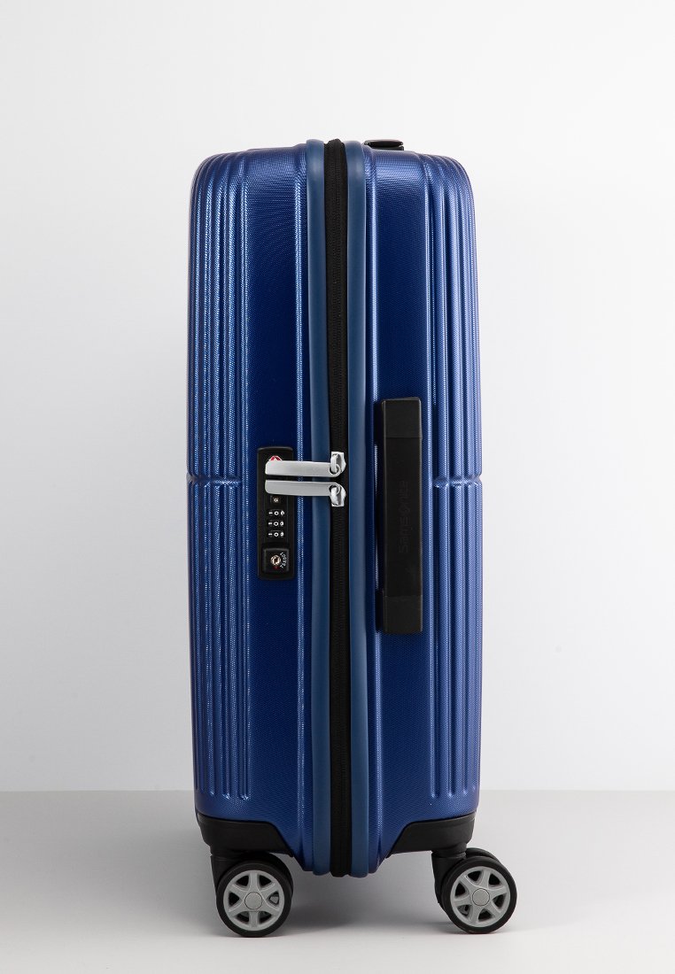 Maleta rígida azul con textura estriada, cerradura de combinación, asa lateral y cuatro ruedas giratorias para facilitar la maniobrabilidad.