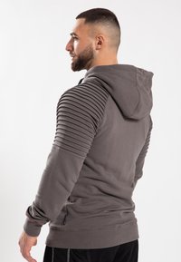 Felpa grigia con accenti a costine sulle spalle, cappuccio regolabile e texture senza cuciture. Stile aderente, tessuto morbido e dettagli con cuciture laterali.