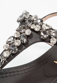 Svart läder sandalett med ett dekorativt band som har grå och klara rhinestones. Slät textur med metalliska accenter och detaljerad sömnad.