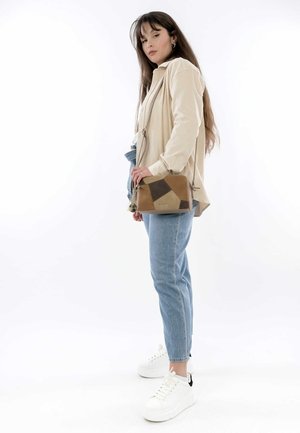 Tan and brown geometric-patterned leather crossbody bag with adjustable strap, held by a person wearing a cream top and light blue jeans.