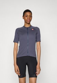 Maillot de cyclisme à manches courtes en bleu marine foncé avec une fermeture éclair à l'avant, en matériau léger, et un petit logo rouge sur la poitrine ; associé à un short de cyclisme noir.