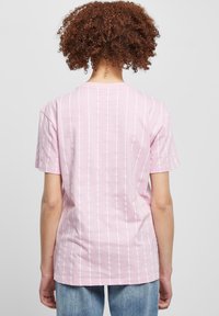 Světle růžové tričko s krátkým rukávem a bílými svislými pruhy, vyrobené z měkké bavlny, s kulatým výstřihem a volným střihem.