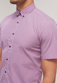 Lyhythihainen, napillinen paita punaisessa ja sinisessä ruutukuviossa, jossa on jämäkkä kaulus ja tummat napit. Sileä, kevyt kangas.