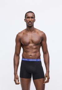 Fekete boxer alsónadrág kék derekú részesedéssel, amelyen a "BJÖRN BORG" szöveg található. Simaságot biztosító anyag, testhezálló kialakítás és minimális varrási részletek jellemzik.