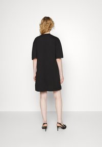 Černé šaty s krátkým rukávem, volného střihu, s kulatým výstřihem a délky do poloviny stehna. Spárované s černými lodičkami na vysokém podpatku.