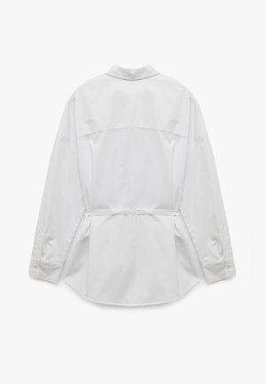 Valkoinen pitkähihaisella paidalla, jossa on selän yoke, napitettu hihansuut ja sidottu vyötärö. Sujuva pinta ja kaareva helma.