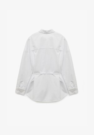 Witte langwerpige blouse met een achterpaneel, knoopmanchetten en een gestrikte taille. Glad oppervlak en ronde onderkant.