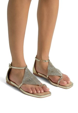 Sandali dorati con un design di strass testurizzati sulla parte superiore del piede, punta aperta e cinturino alla caviglia, suola piatta e forma minimalista.